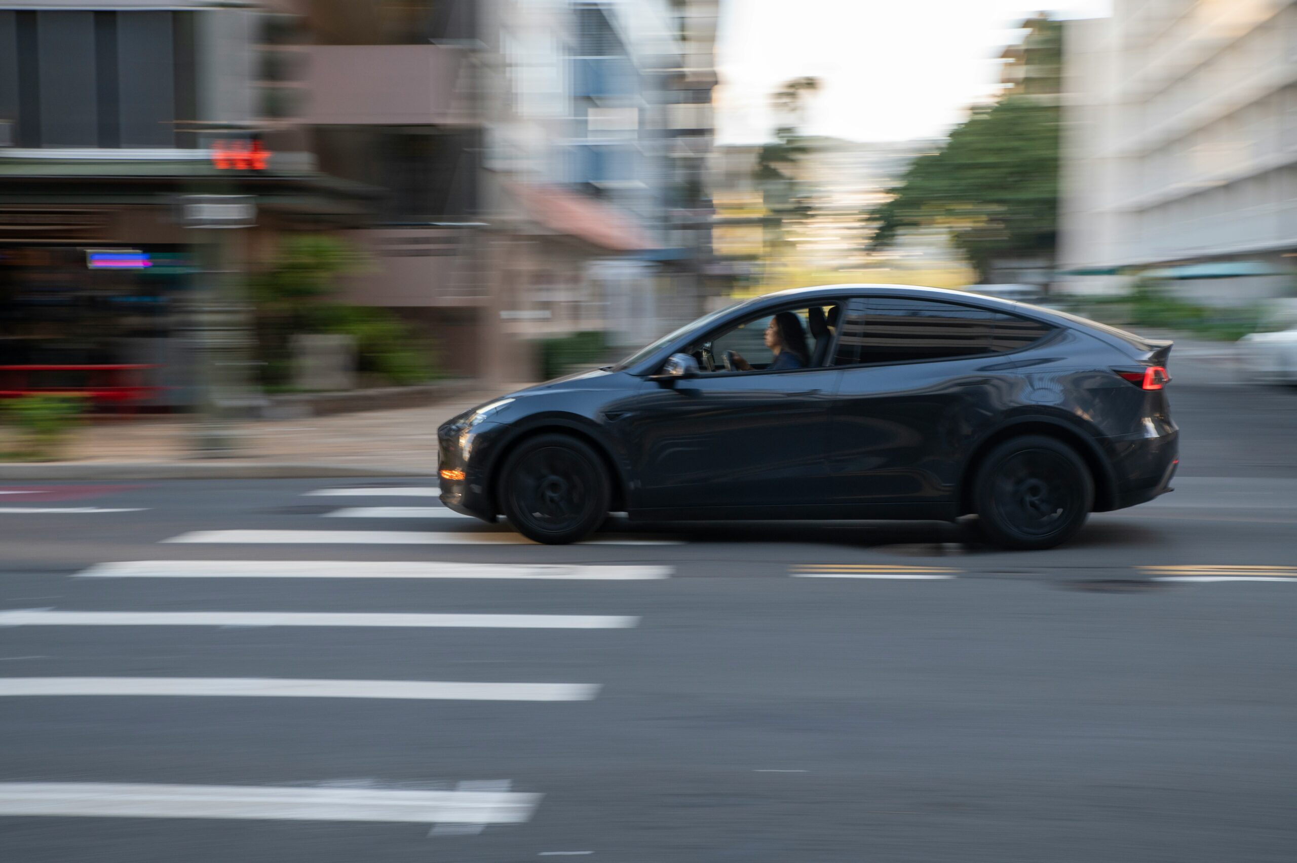 Dark car driving through a city crosswalk at night, evoking Waymo robotaxi rides and autonomous vehicle safety technology.