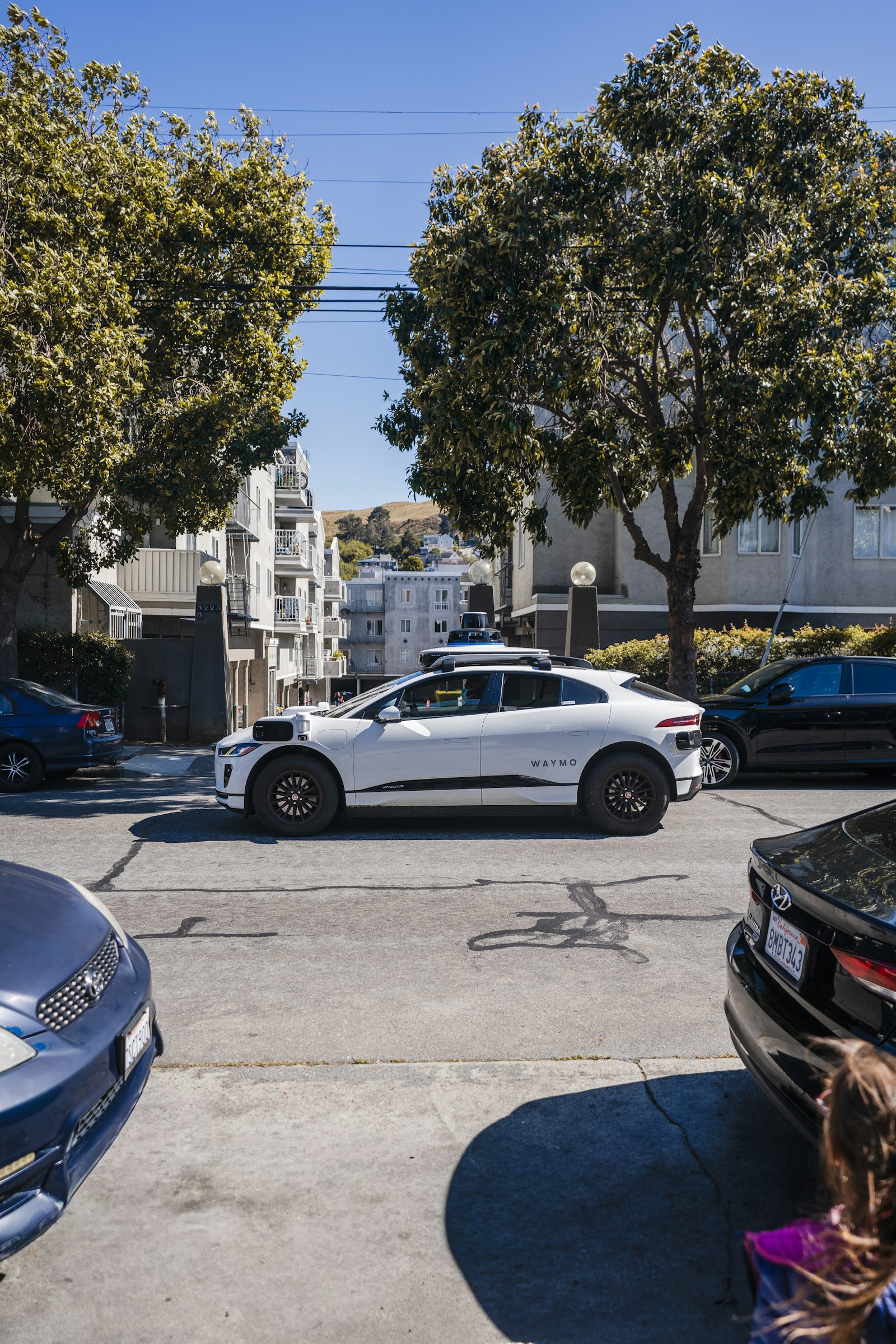 White self-driving car on a city street, representing the new Zoox airport robotaxi service