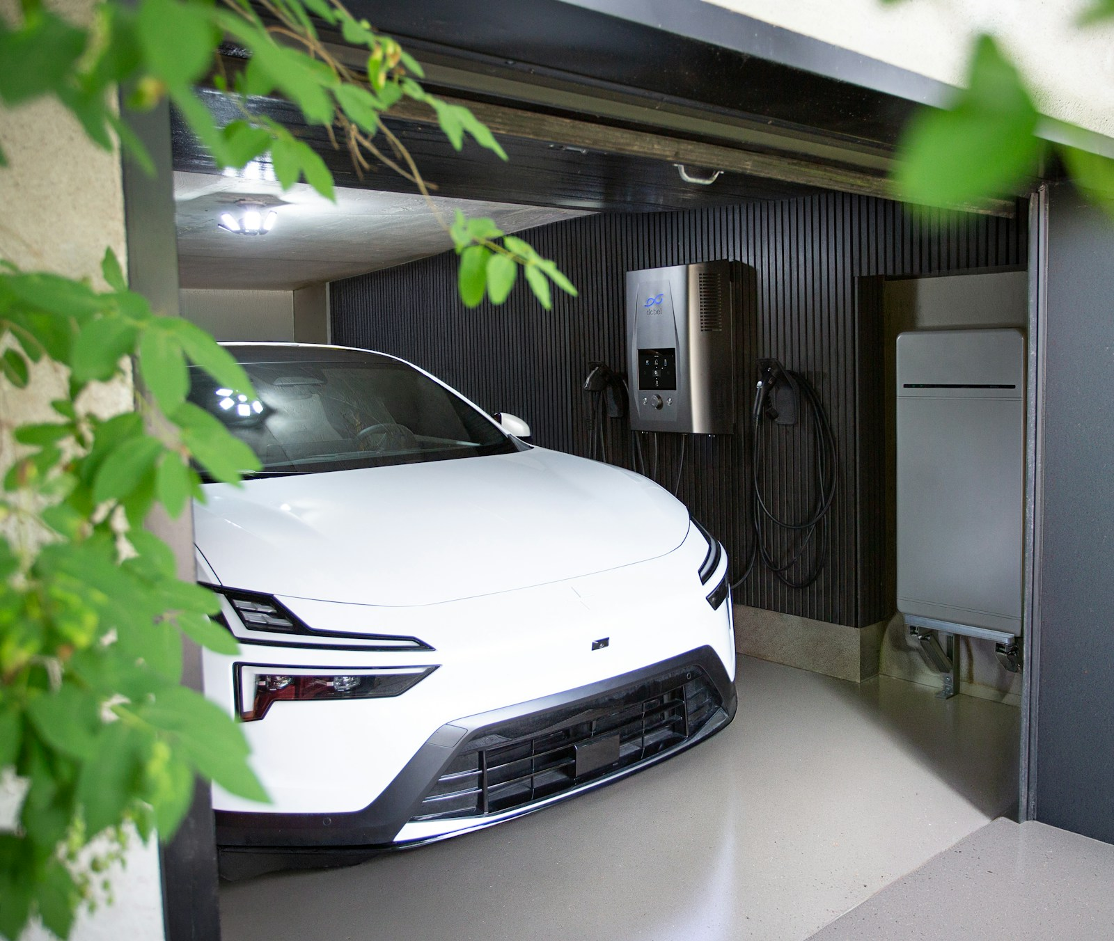 A wall-mounted home energy station in a garage with an electric car, linking home battery storage to the grid