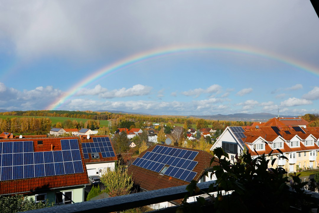 Rooftop solar panels on homes under a rainbow, illustrating free solar battery savings for UK households