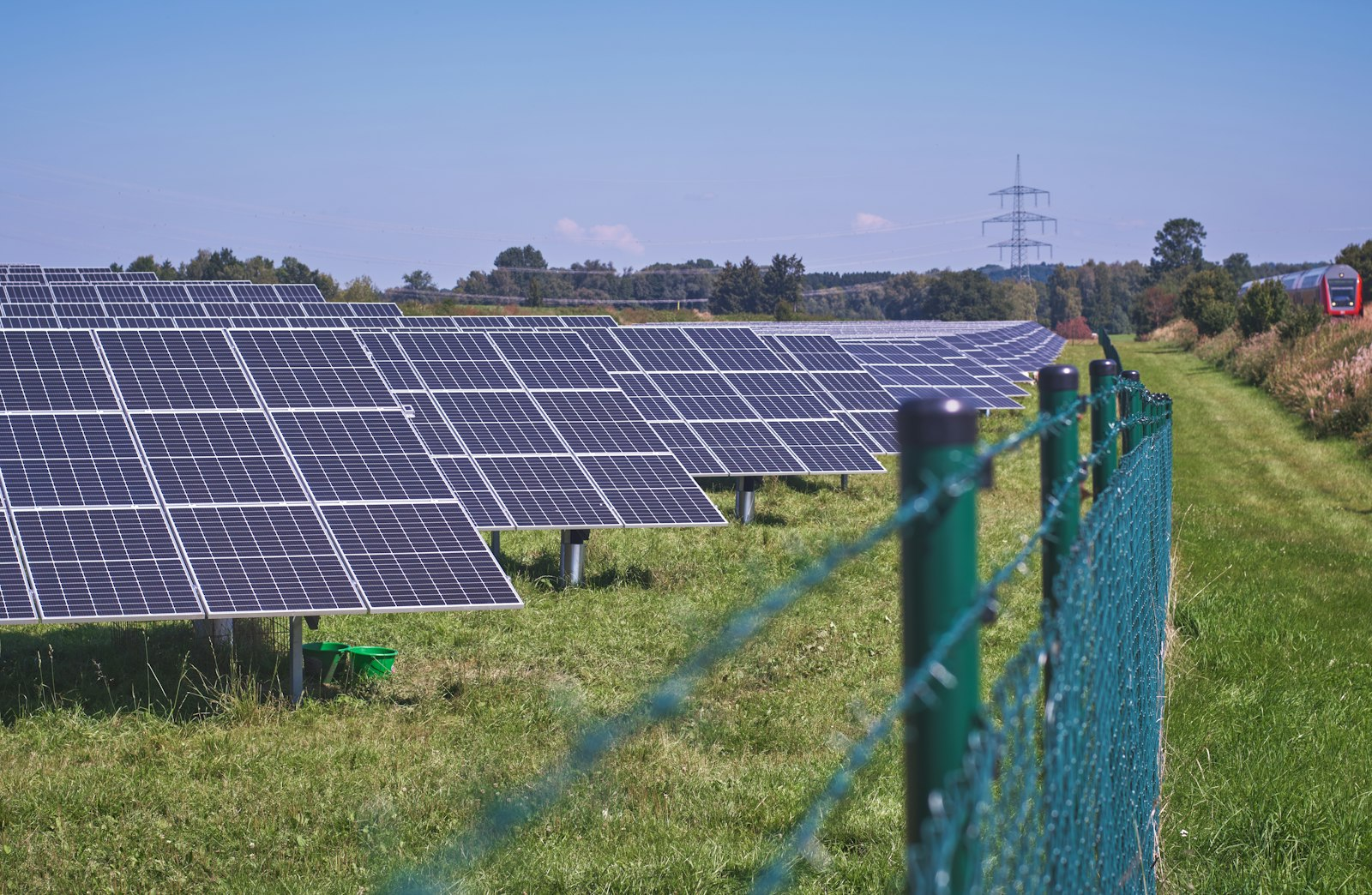 Rows of ground-mounted solar panels on a grass field under a blue sky